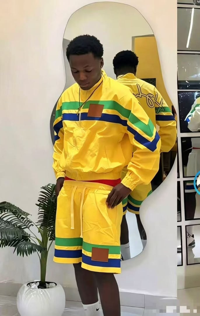 Model wearing yellow striped windbreaker jacket and shorts with green blue stripes and brown patches.