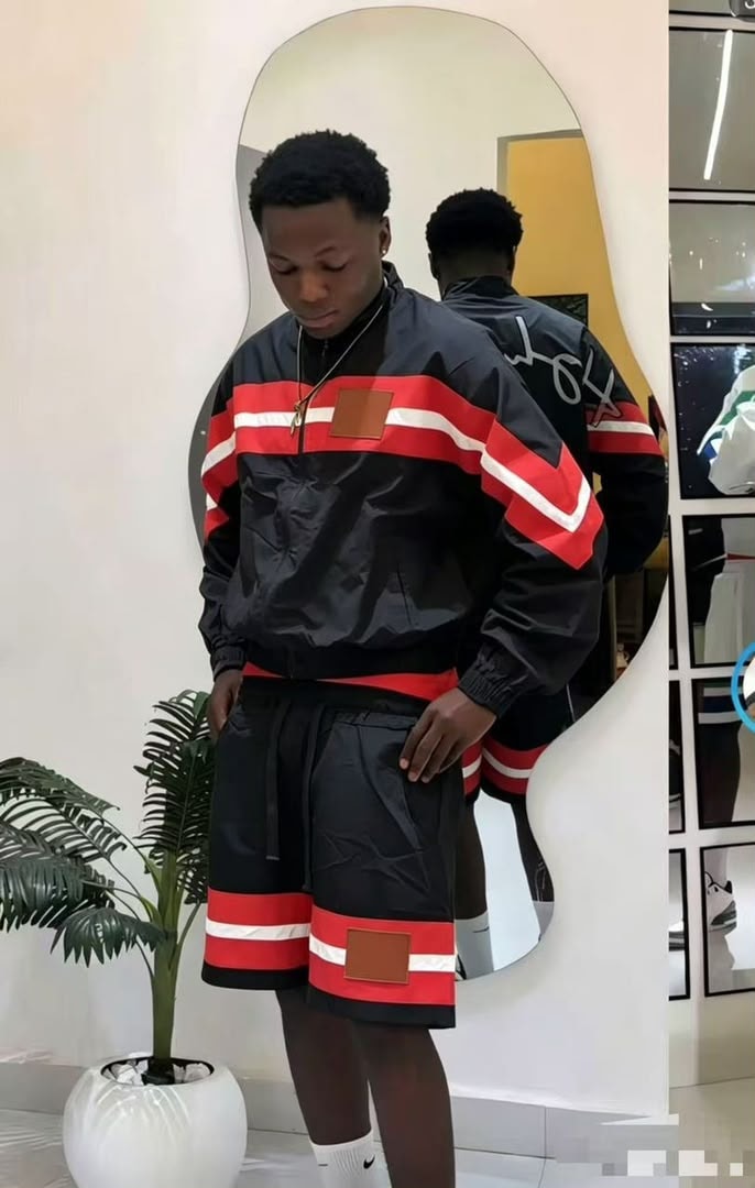 Model wearing black striped windbreaker jacket and shorts with red white stripes and brown patches.