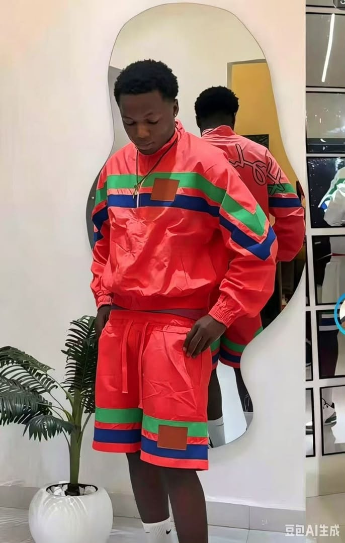 Model wearing red striped windbreaker jacket and shorts with green blue stripes and brown patches.
