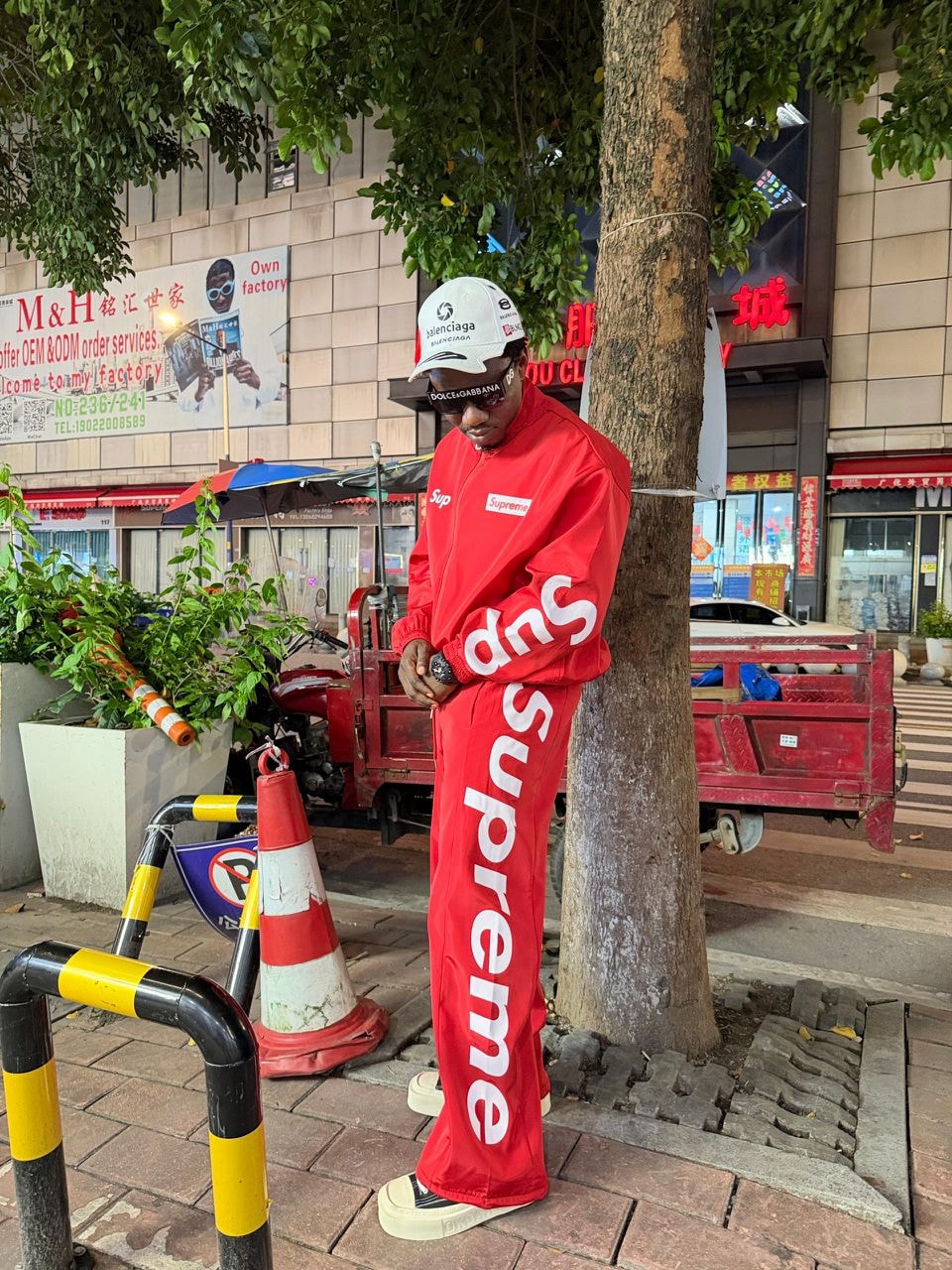 Model wearing red Supreme two-piece tracksuit with white branding outdoors.