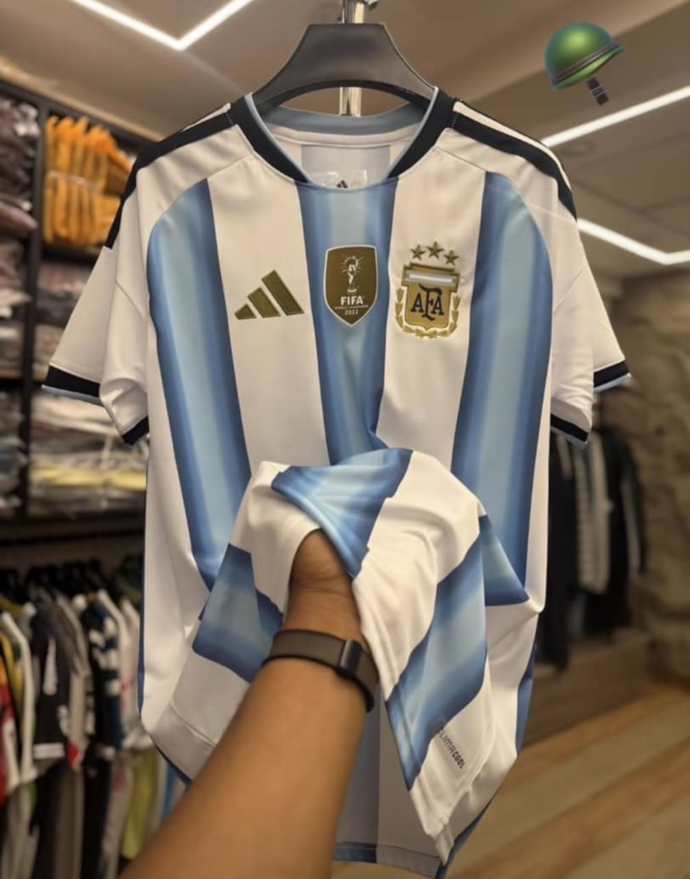 White and blue striped Adidas Argentina football jersey held in store.