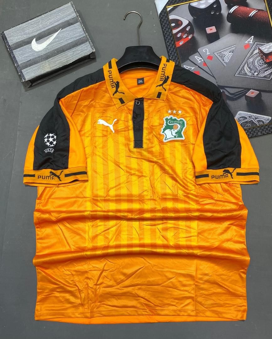 Orange and black Puma Cote d'Ivoire football jersey on hanger with accessories.