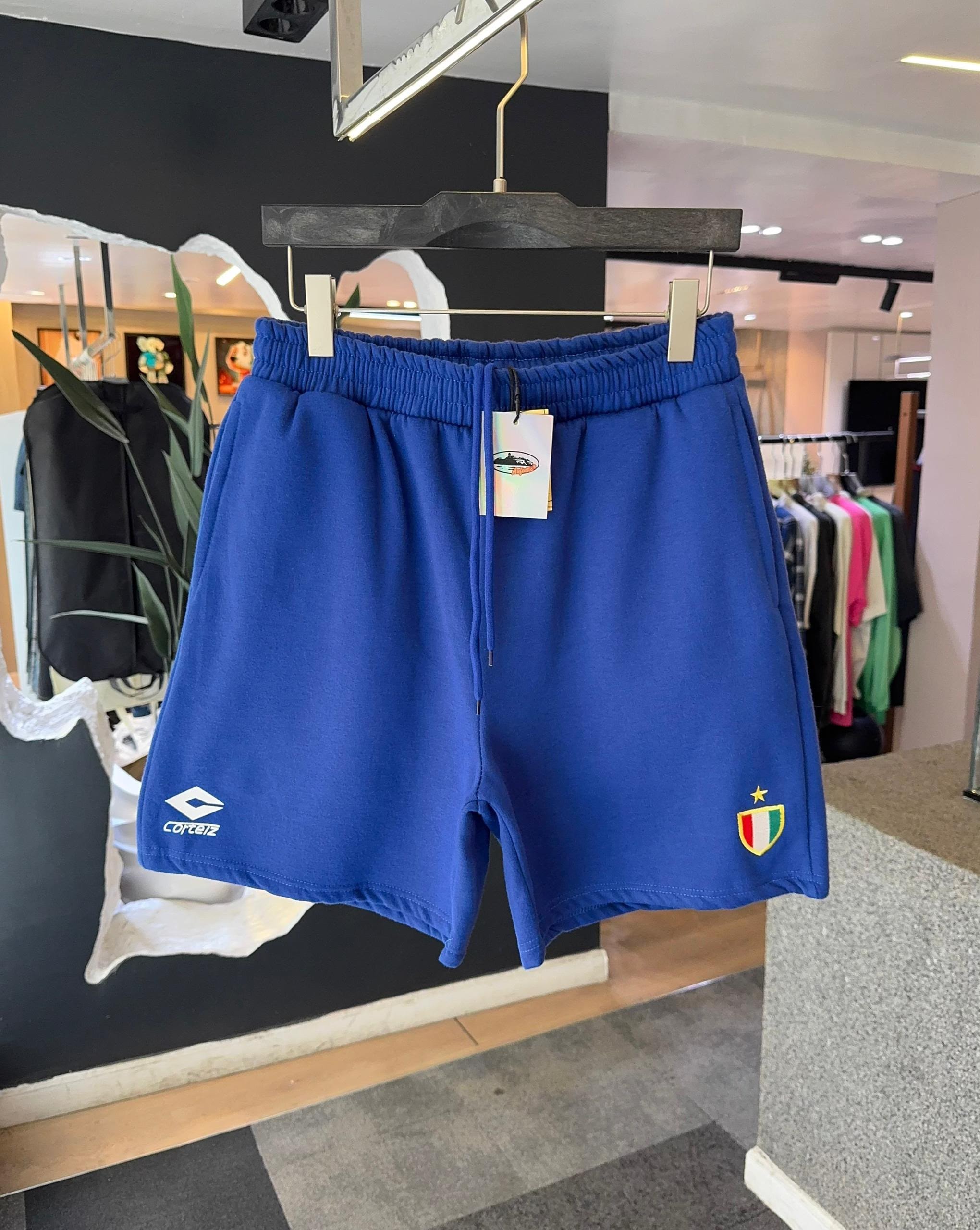 Blue Corteiz fleece shorts with logo and crest hanging in store.