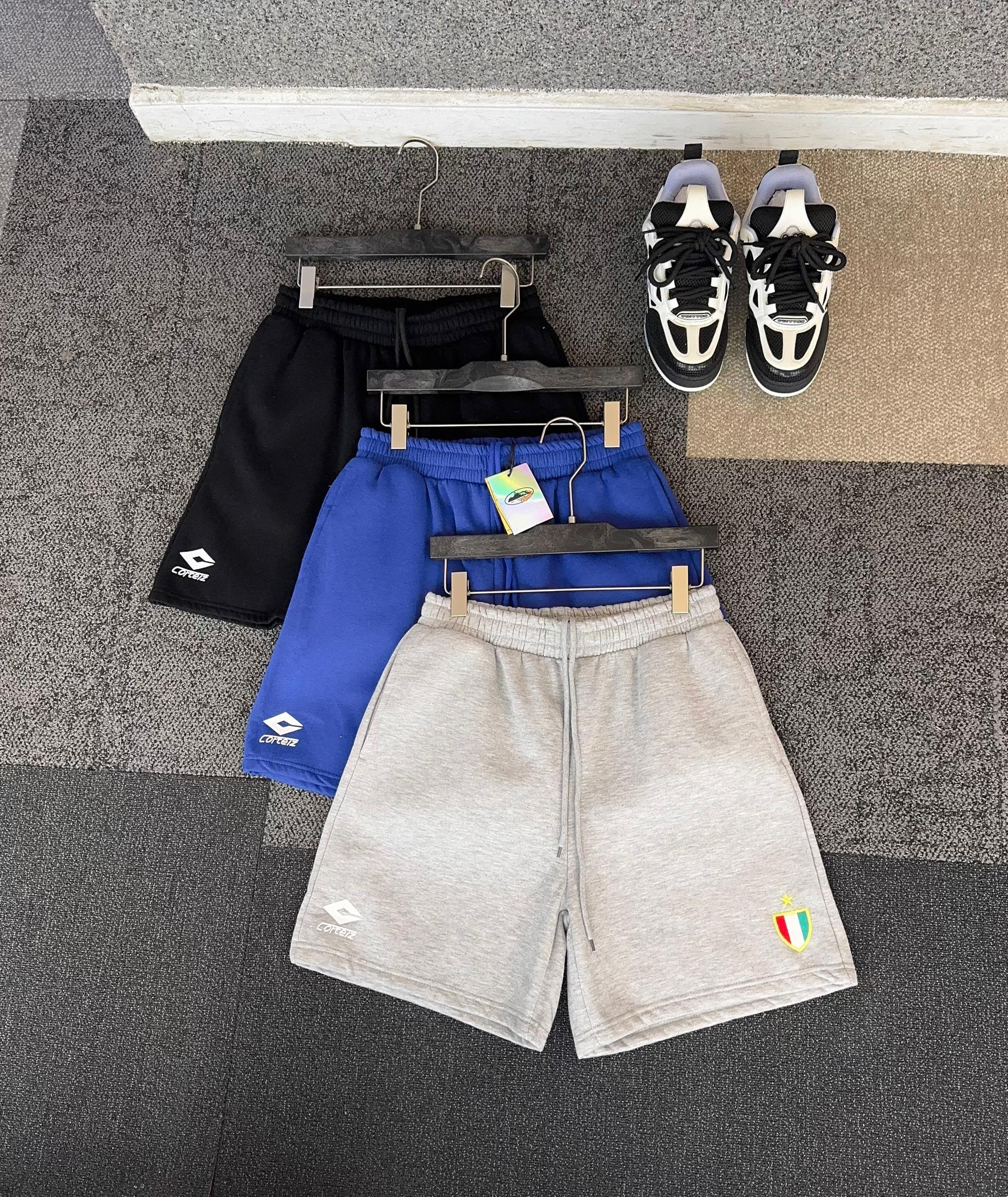 Corteiz shorts in black, blue, and gray laid flat with sneakers above.