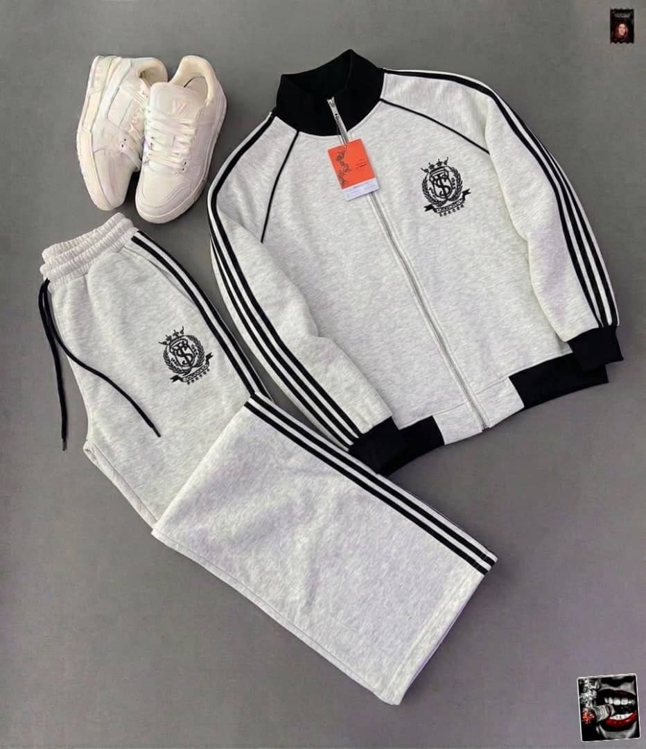 White tracksuit with crest logo, black stripes on zip jacket and pants, styled with white sneakers.