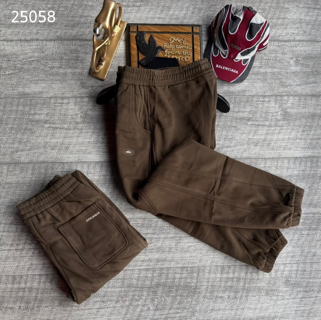 Brown ALO joggers laid out showing front logo view and folded to display back pocket on gray surface.