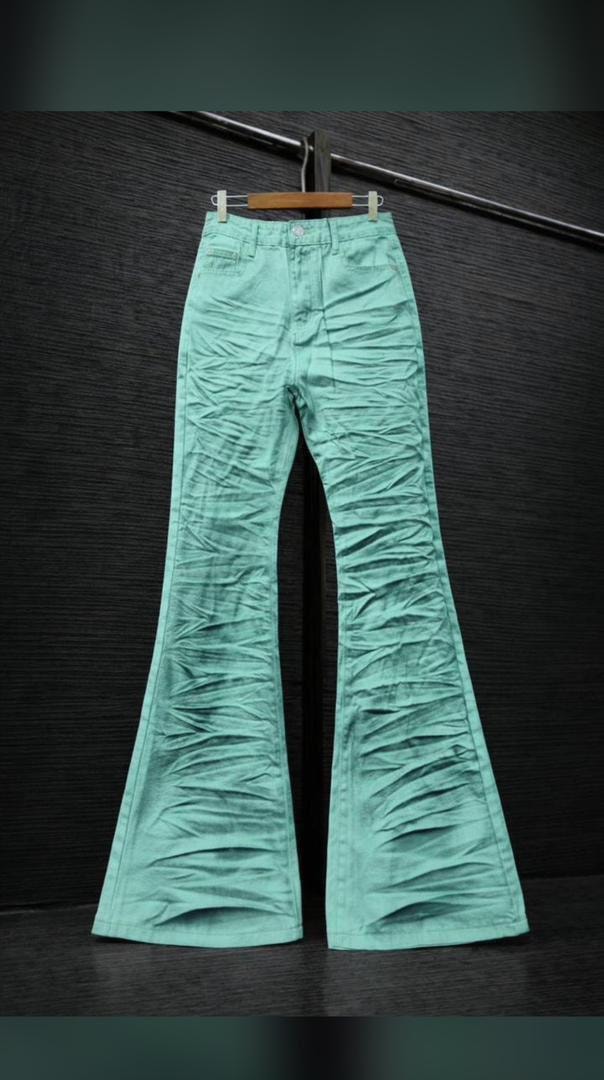 Green ruched flare jeans hanging on wooden hanger against dark background.