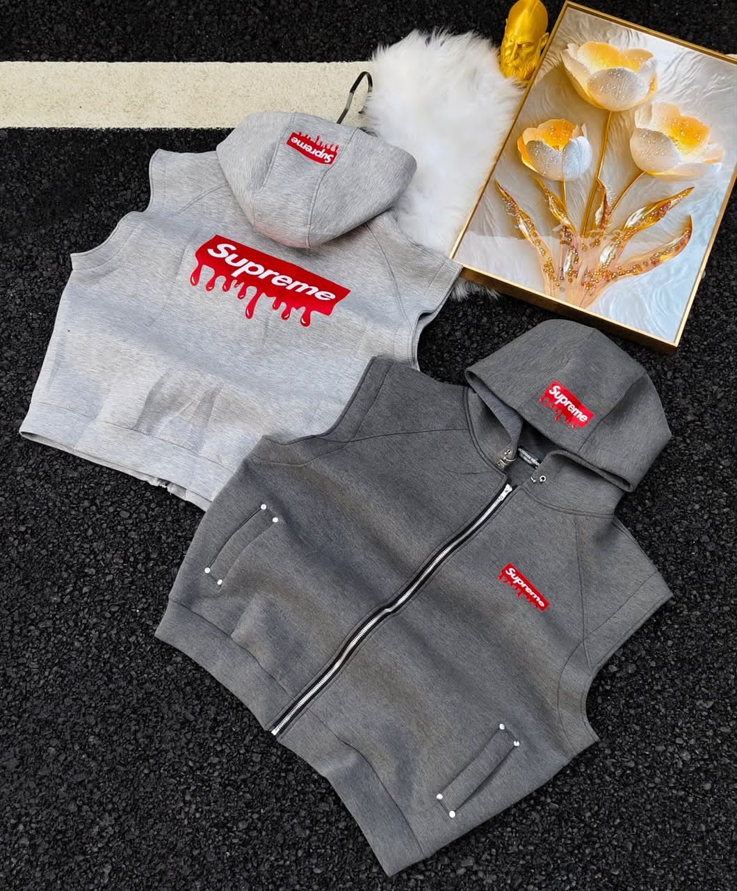 Supreme logo sleeveless hoodies in light and dark gray with golden floral decor and white fur.