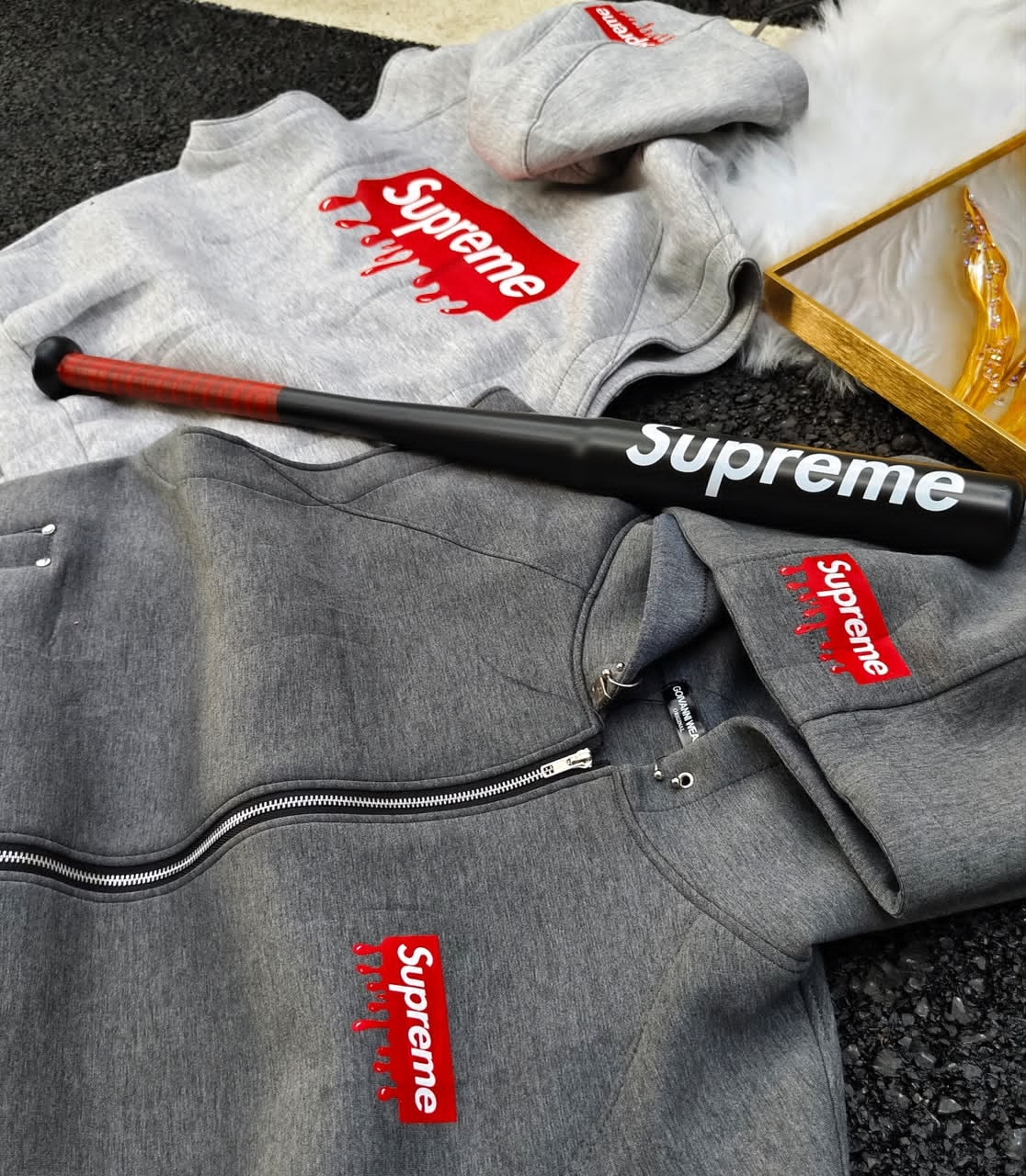 Supreme box logo hoodies in light and dark gray with branded baseball bat and gold decor.