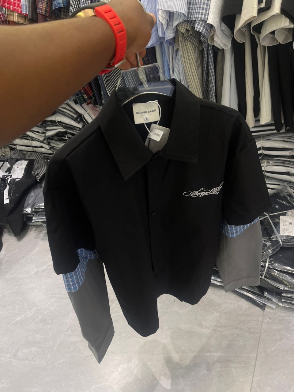 Front view of black short sleeve collared shirt with white chest embroidery and contrasting cuffs, held on a hanger in a store.
