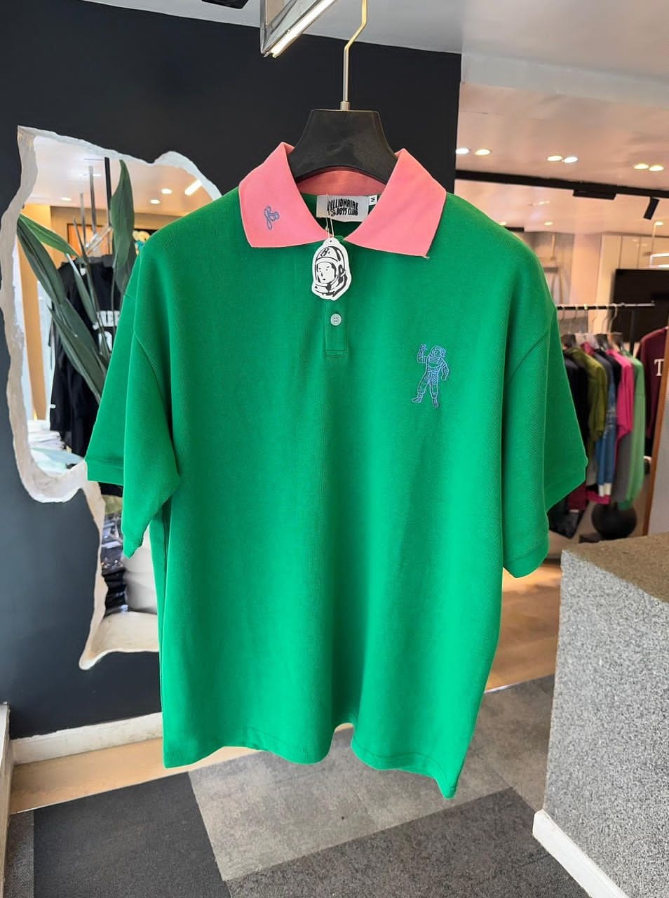 Green Billionaire Boys Club polo with pink collar and blue astronaut embroidery on chest.