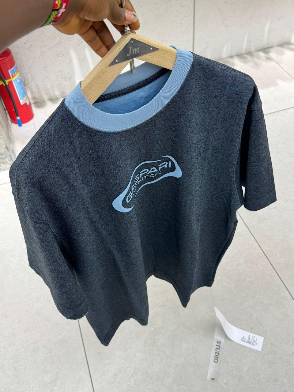 Dark gray Gaspari polo shirt with light blue ribbed collar, cuffs, and chest logo, hanging on a wooden hanger.