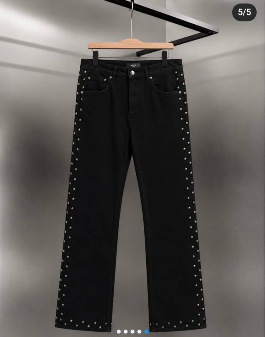 Black jeans with silver star studs along the side seams hanging on wooden hanger.