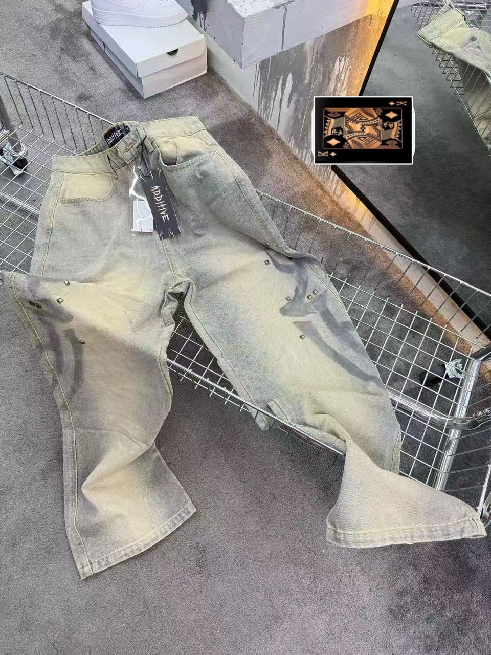 Beige faded baggy jeans with studs and tags displayed in metal cart.