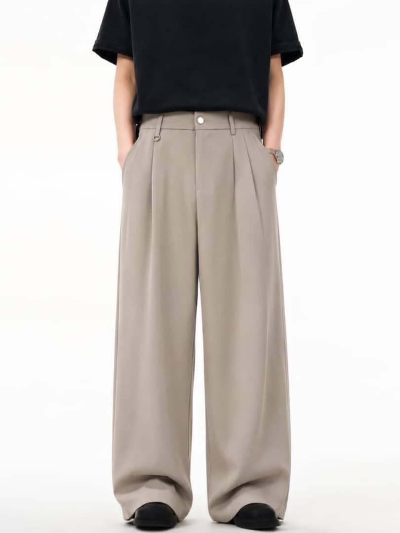 Model wearing beige pleated flare trousers with hands in pockets.