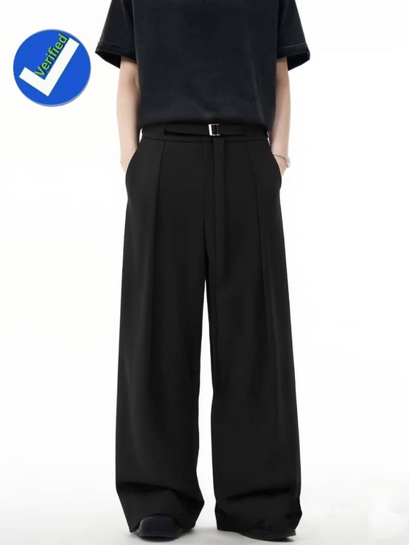 Model wearing black pleated flare trousers with belt and hands in pockets.