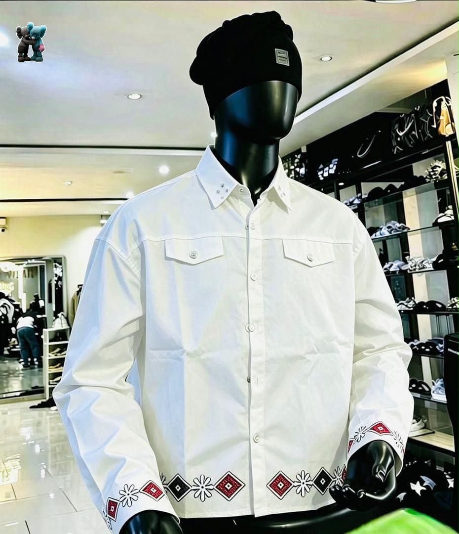 White long sleeve button-up shirt with embroidery on cuffs and hem, displayed on mannequin with black beanie.
