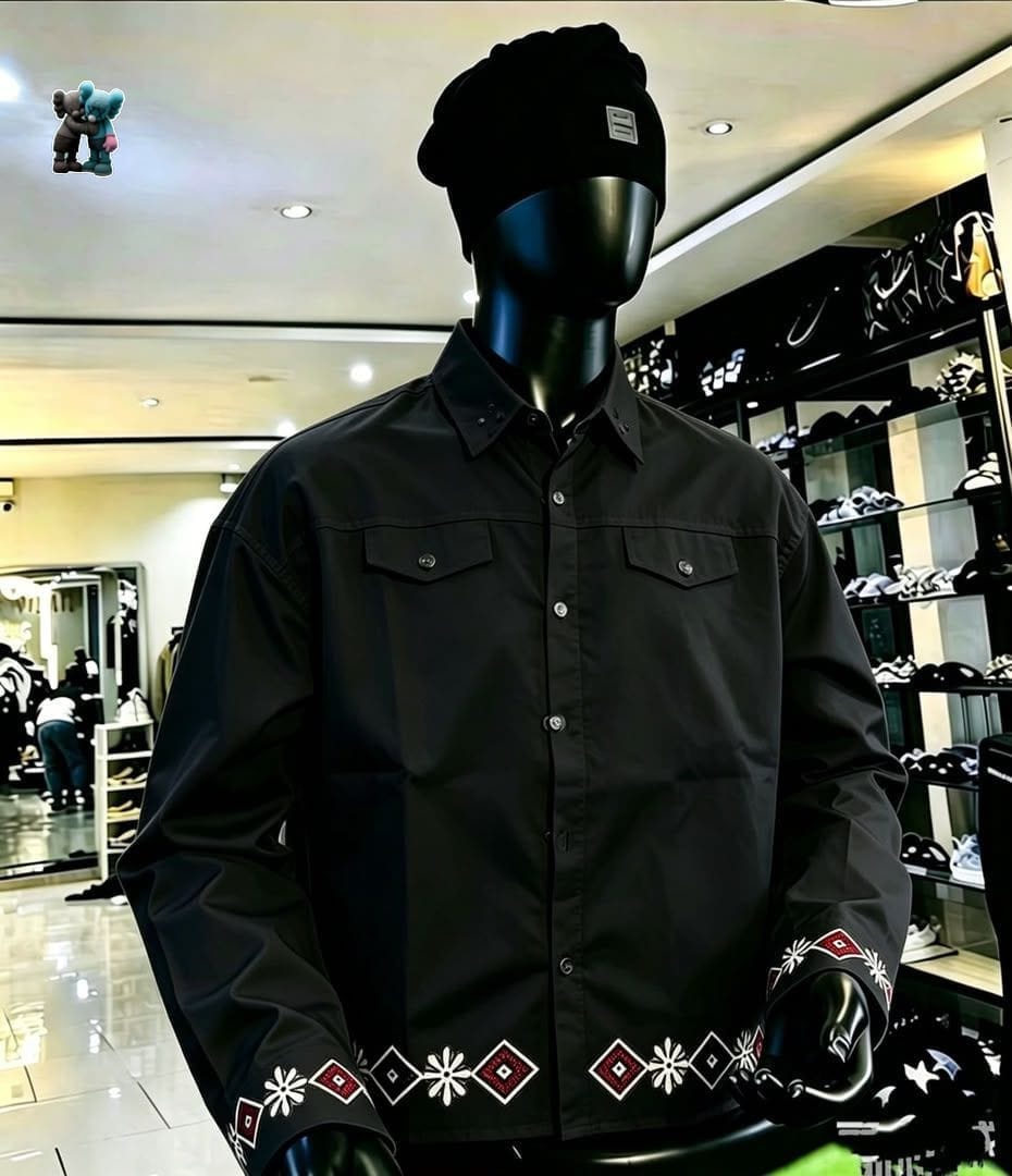 Black long sleeve button-up shirt with embroidery on cuffs and hem, displayed on mannequin with black beanie.