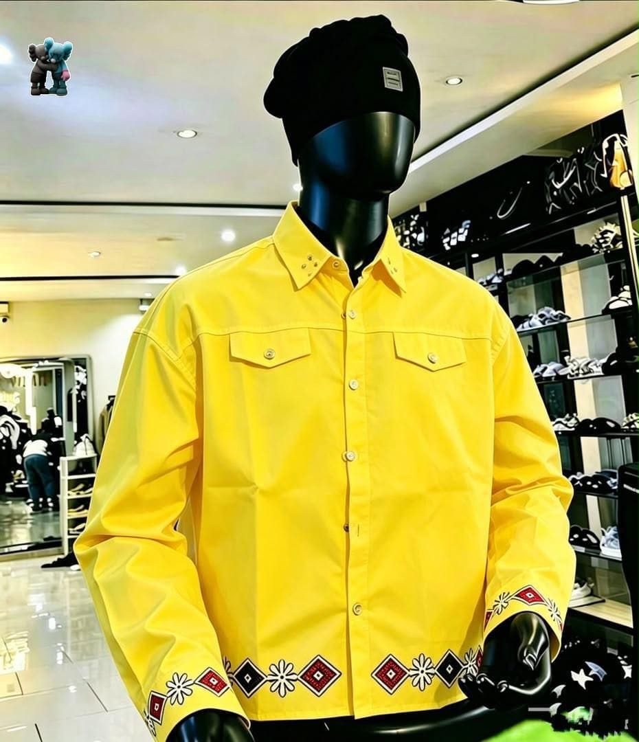 Yellow long sleeve button-up shirt with embroidery on cuffs and hem, displayed on mannequin with black beanie.