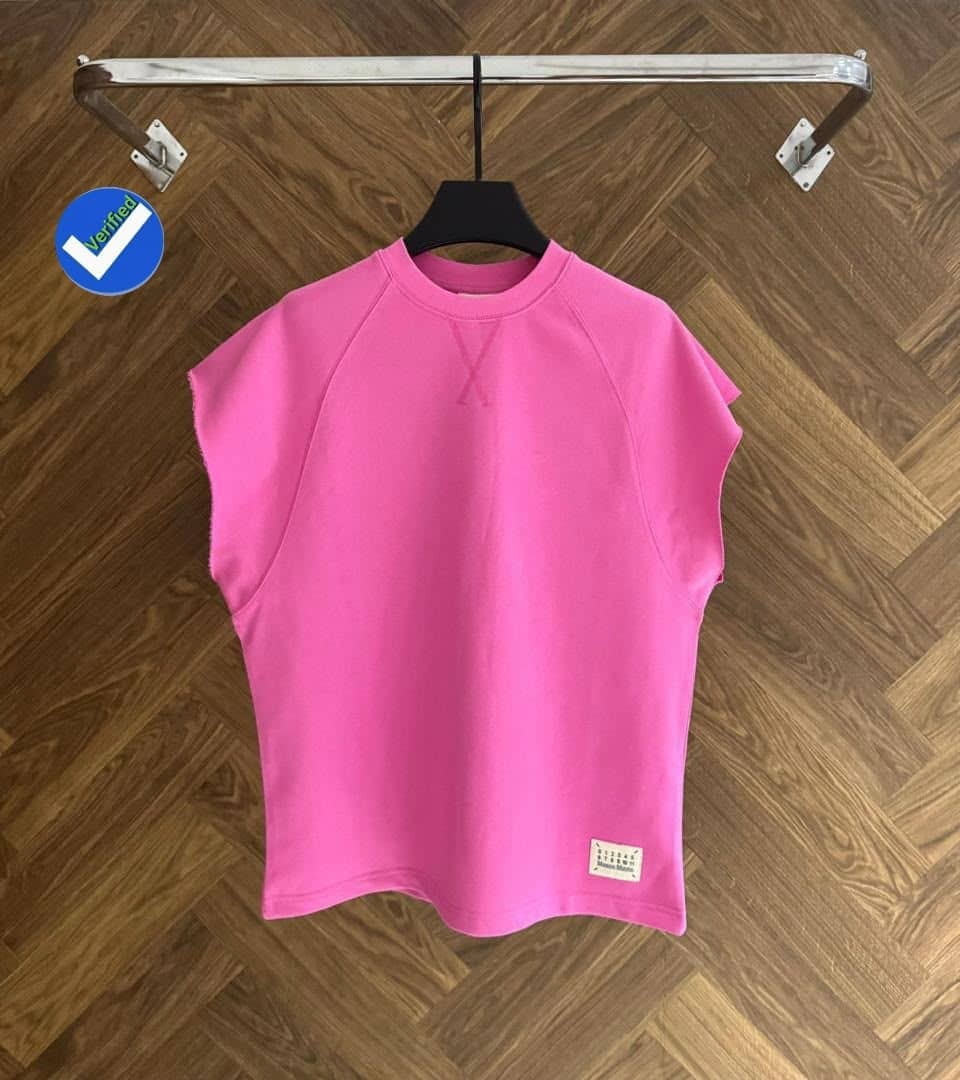Bright pink armless raglan top on hanger against wooden floor.