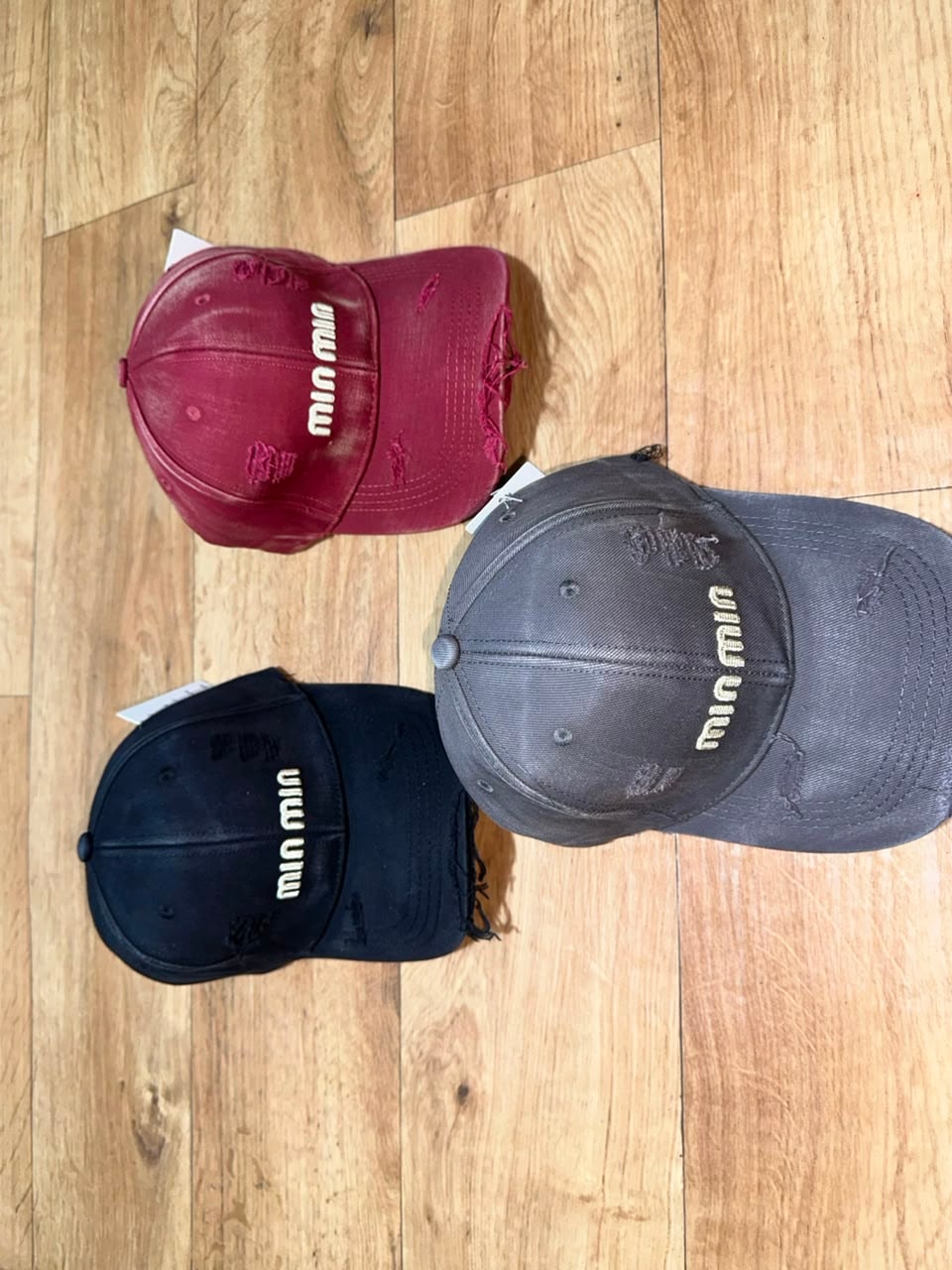 Distressed Miu Miu baseball caps in maroon, gray, and black with text embroidery.