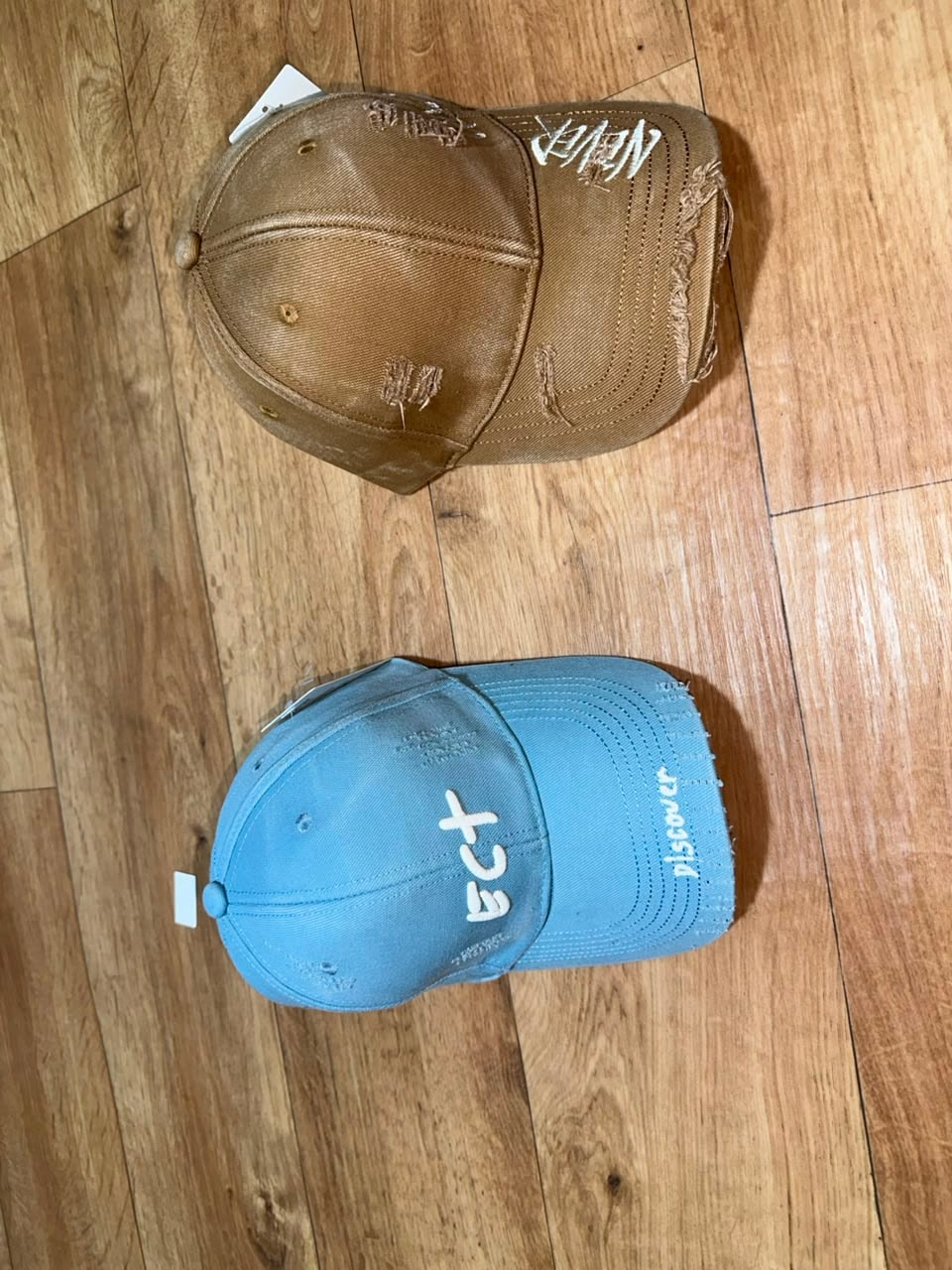 Distressed printed baseball caps in brown and light blue with text details.