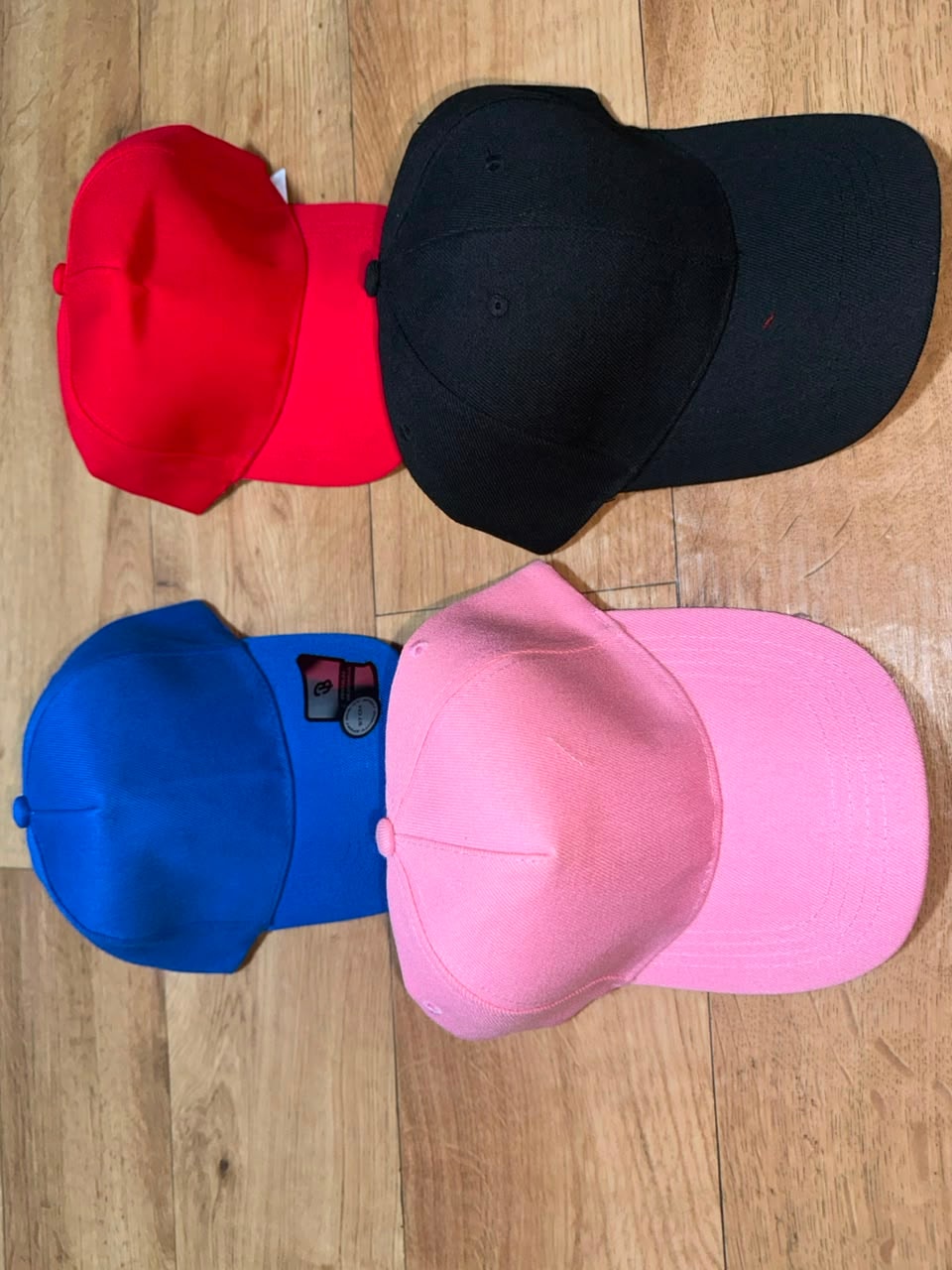 Plain baseball caps in red, black, blue, and pink colors.