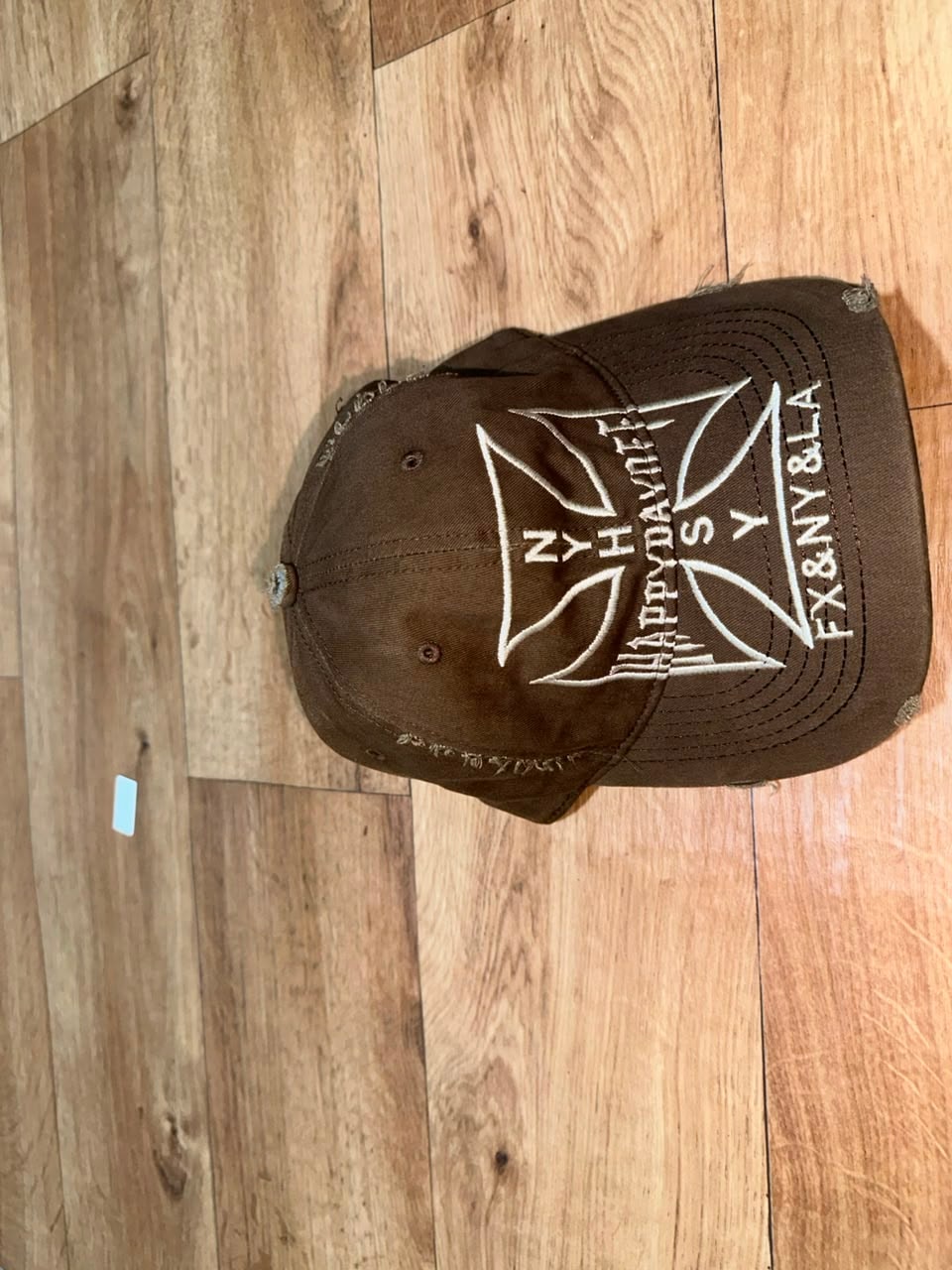 Brown distressed baseball cap with white embroidered cross and text graphics.
