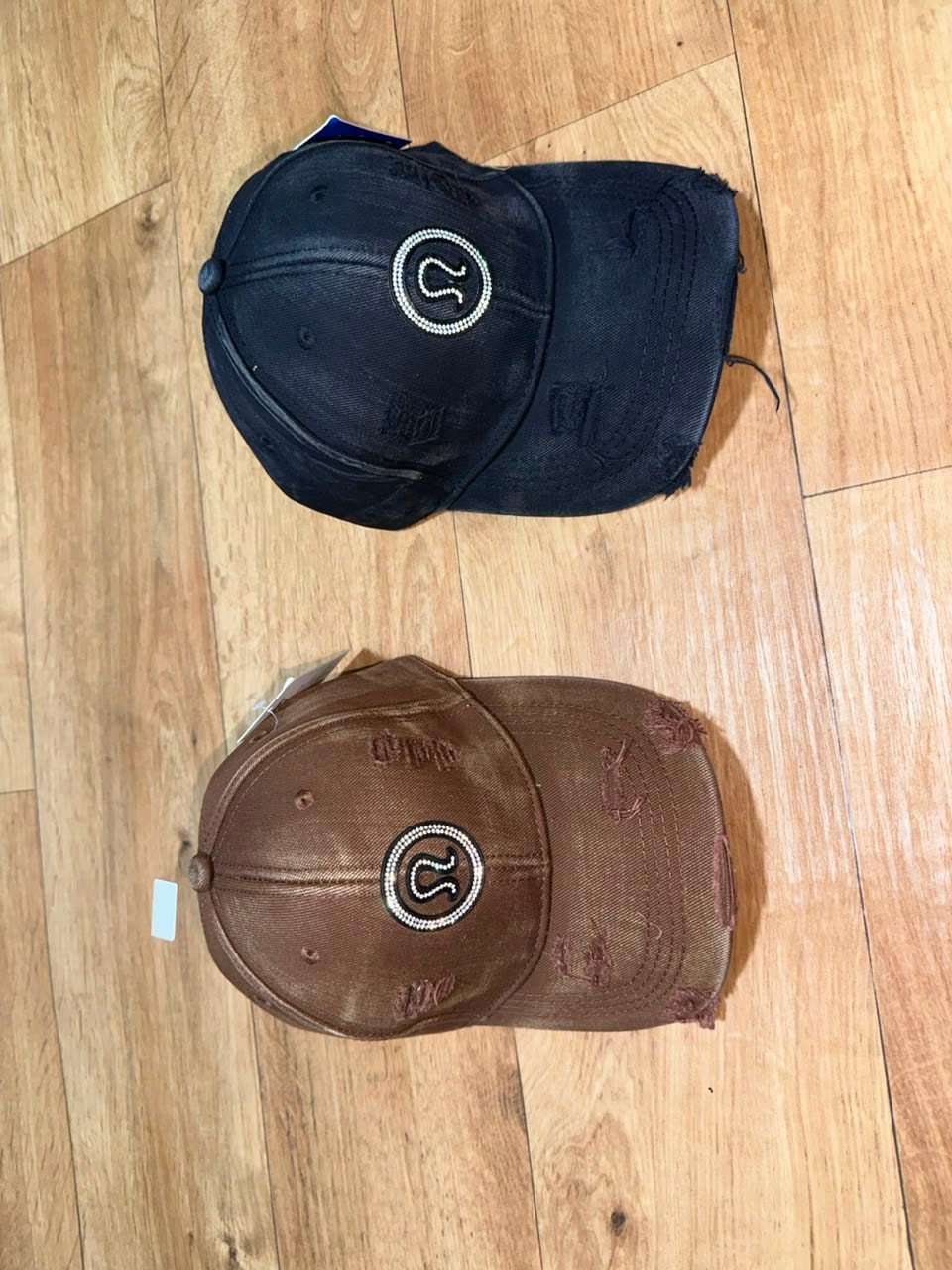 Distressed caps with circular beaded logo in black and brown colors.