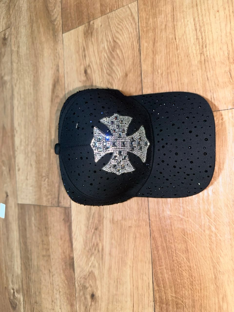 Black perforated baseball cap with large silver rhinestone cross emblem.