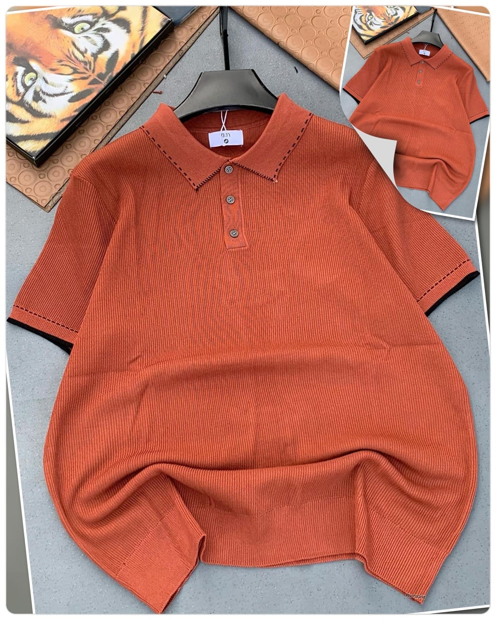 Orange ribbed polo shirt with black contrast stitching on collar and cuffs, laid flat on gray surface with inset view.