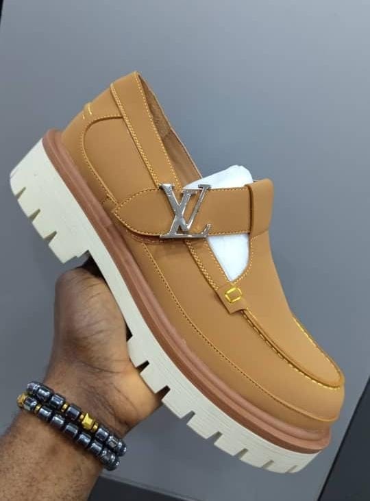Tan Louis Vuitton loafers with silver LV buckle held in hand.
