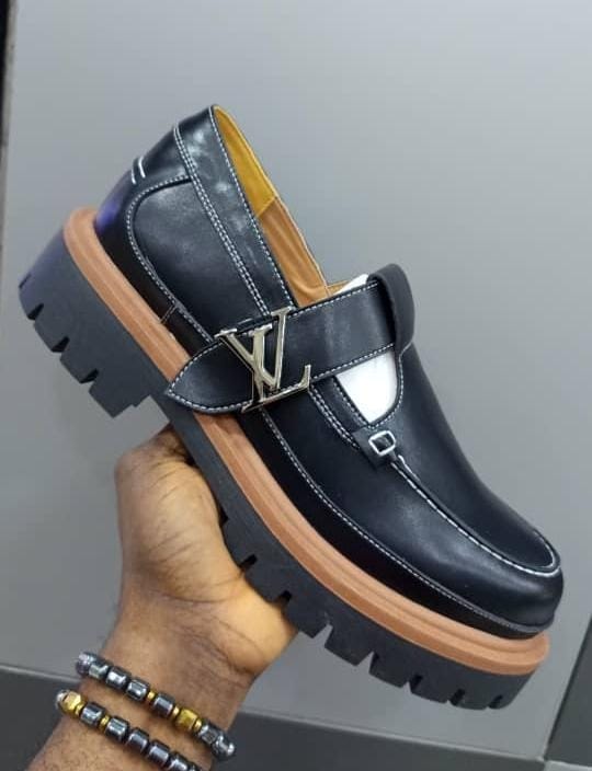 Black Louis Vuitton loafers with LV buckle held in hand showing side profile.