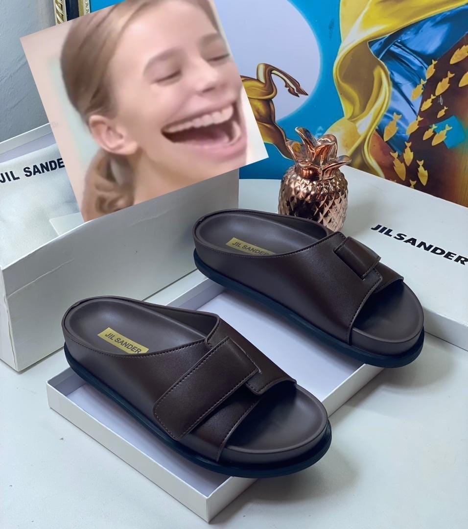 Brown Jil Sander slides displayed in white box with lifestyle props.