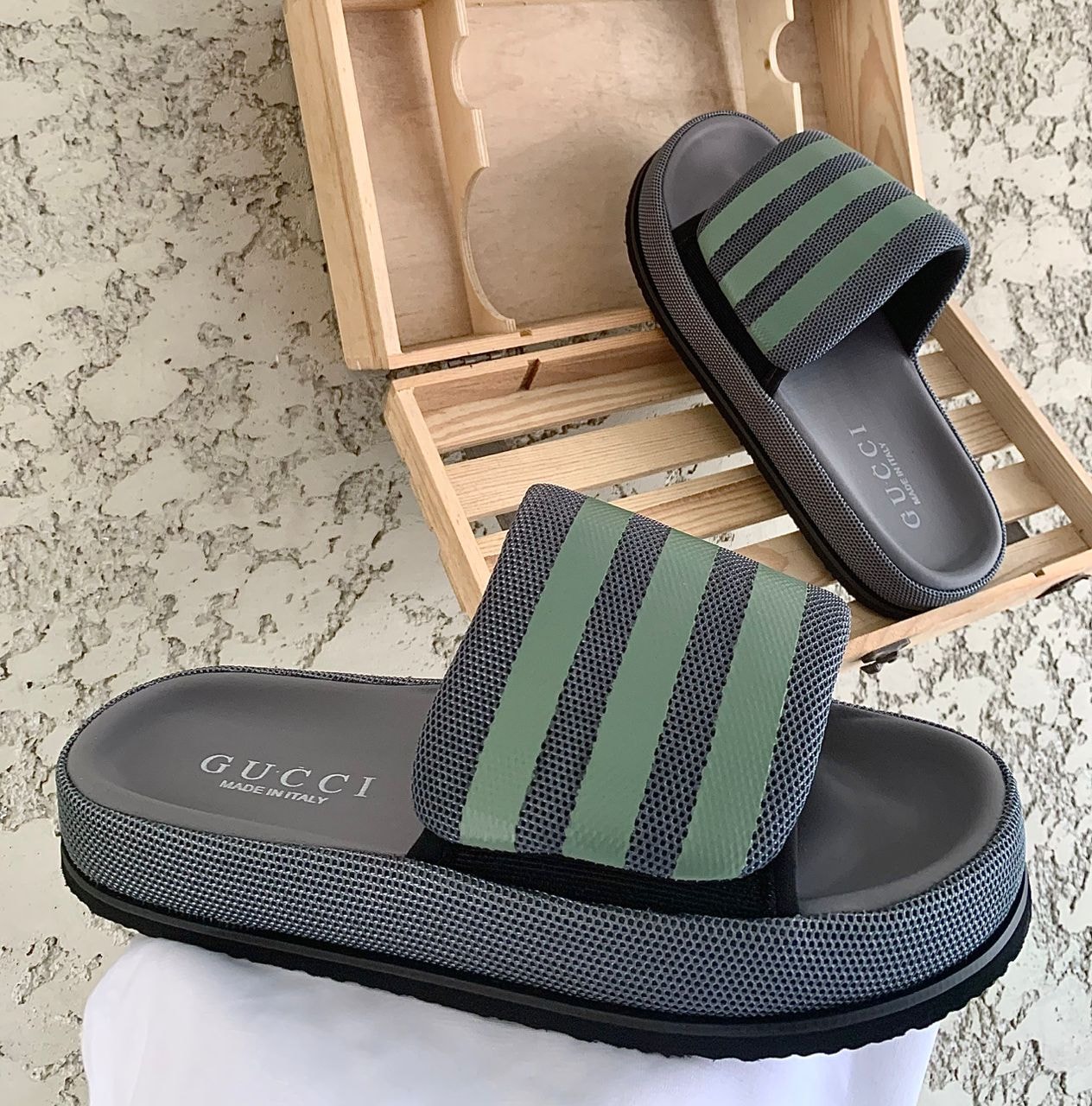 Gucci green and gray striped slides on wooden crate and white fabric.