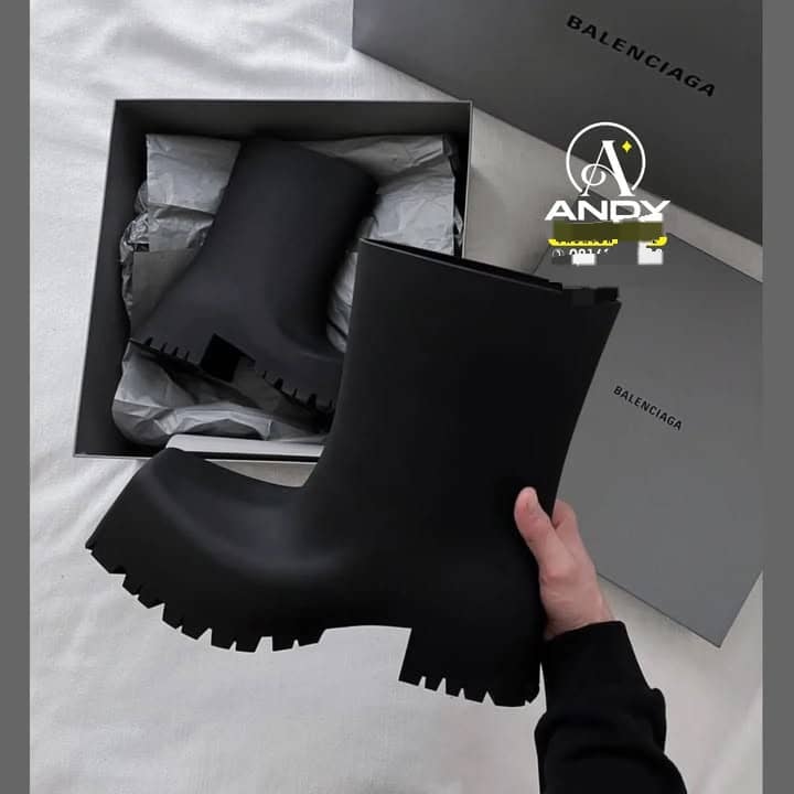 Hand holding black Balenciaga boot removed from branded box with tissue paper.