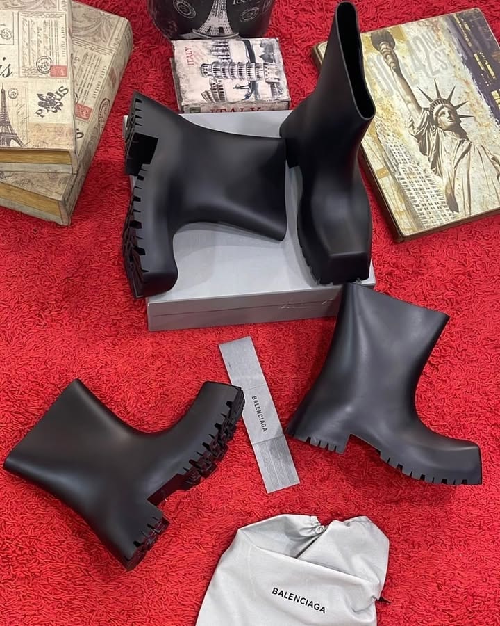 Black Balenciaga rubber ankle boots displayed in various views with branding accessories on red background.