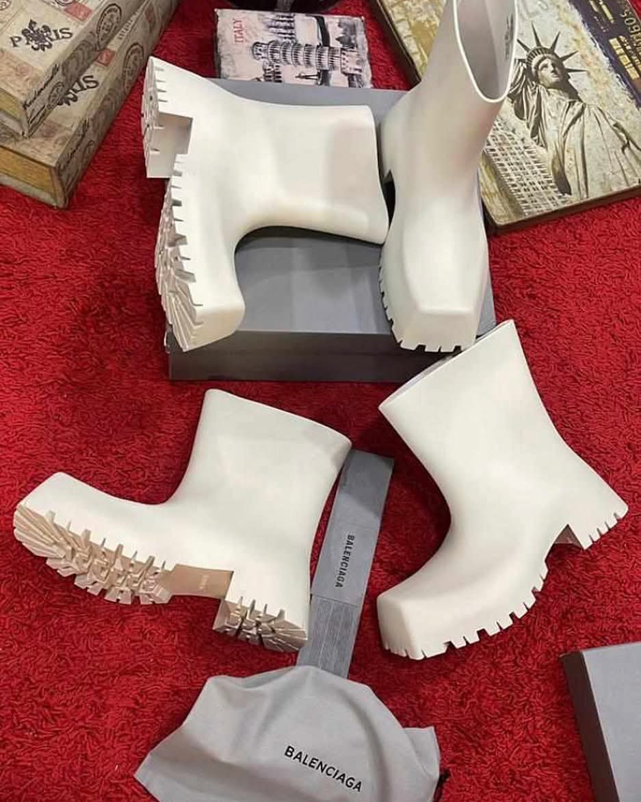 White Balenciaga rubber ankle boots shown from multiple angles on red surface with boxes and dust bag.