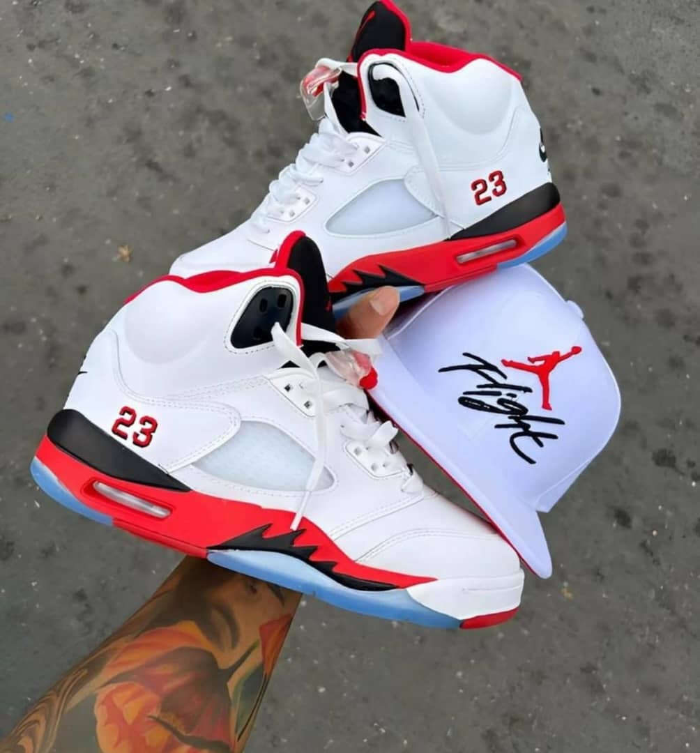 White red and black Air Jordan 5 sneakers held with a white Flight cap.