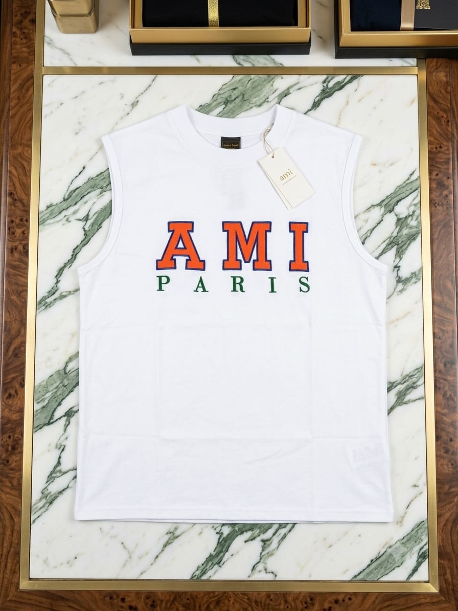 White AMI Paris sleeveless t-shirt with orange and green logo laid flat on marble surface.