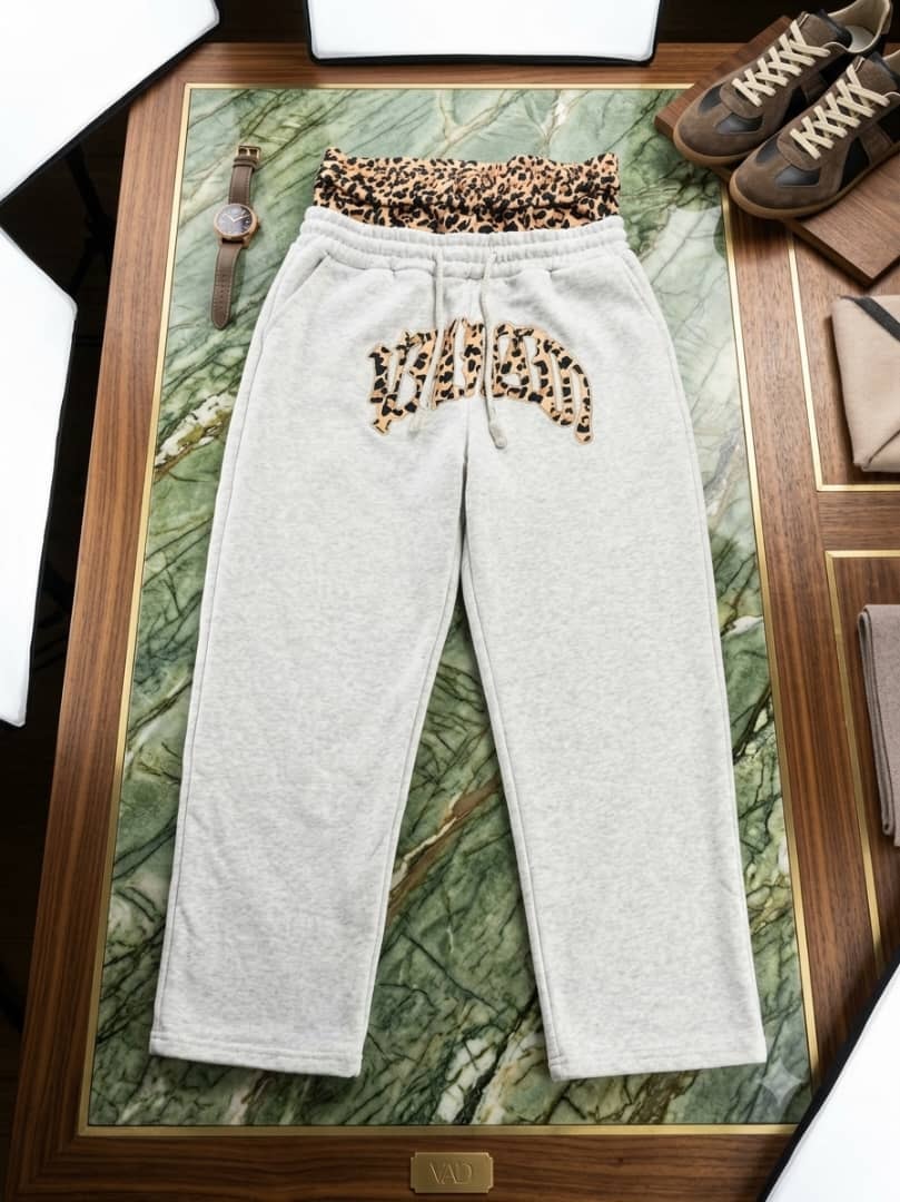 Gray joggers with leopard print waist and logo on green marble.