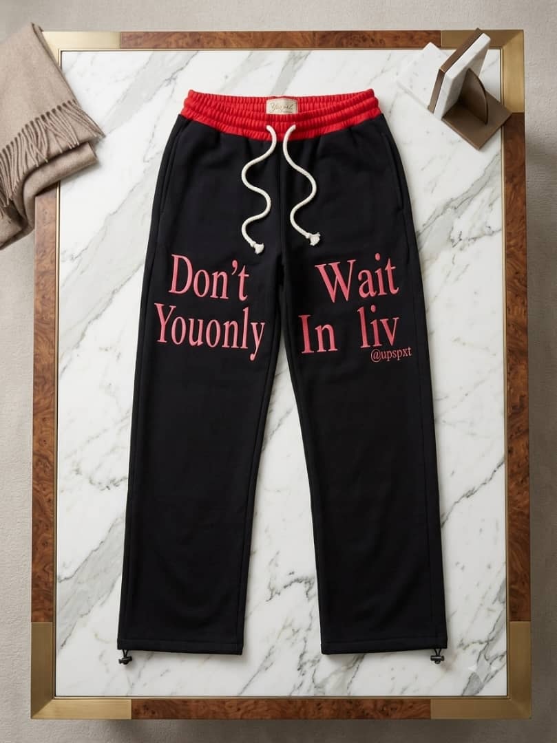 Black joggers with pink text and red waistband on marble.