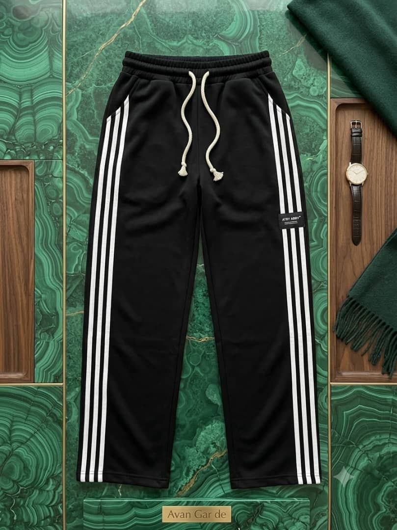 Black joggers with white triple side stripes on green marble.