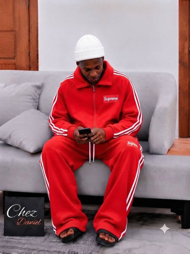 Model wearing red Supreme zip-up tracksuit with white stripes.