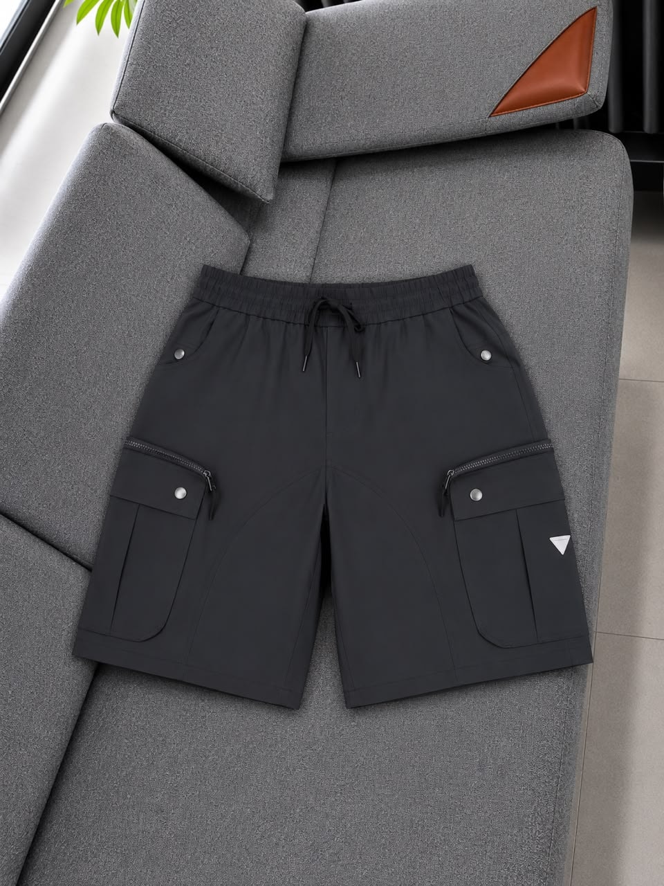 Dark gray cargo shorts with triangle logo on sofa.