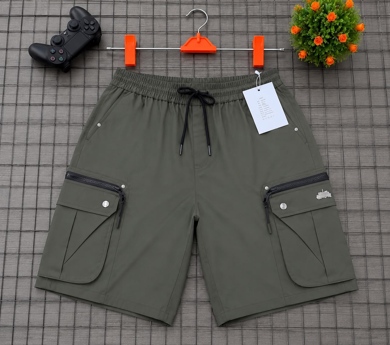Olive cargo shorts on grid background with hanger, game controller and plant accessory.