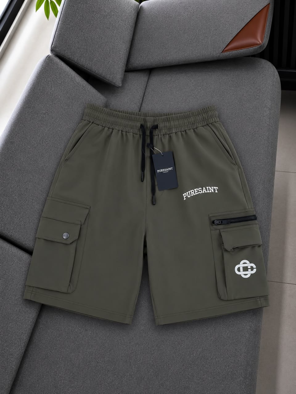 Olive Puresaint cargo shorts on gray sofa showing leg print, logo and tag.
