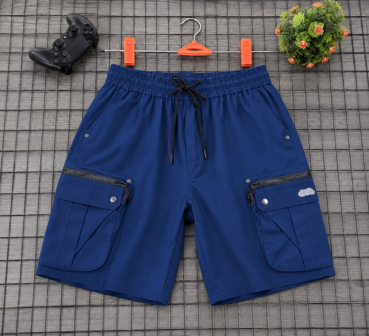 Blue cargo shorts hung on orange clips against grid background with game controller and plant.