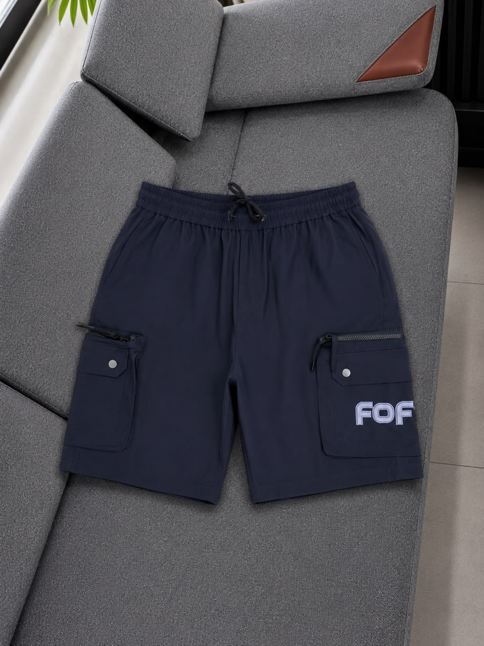 Navy FOF cargo shorts laid on gray sofa showing side pockets and logo.