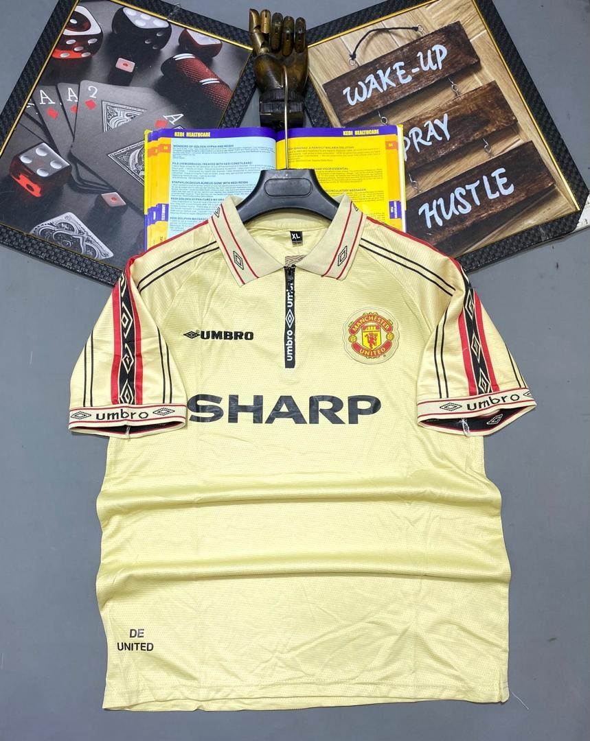 Cream yellow retro Manchester United Umbro jersey hanging with background decor.